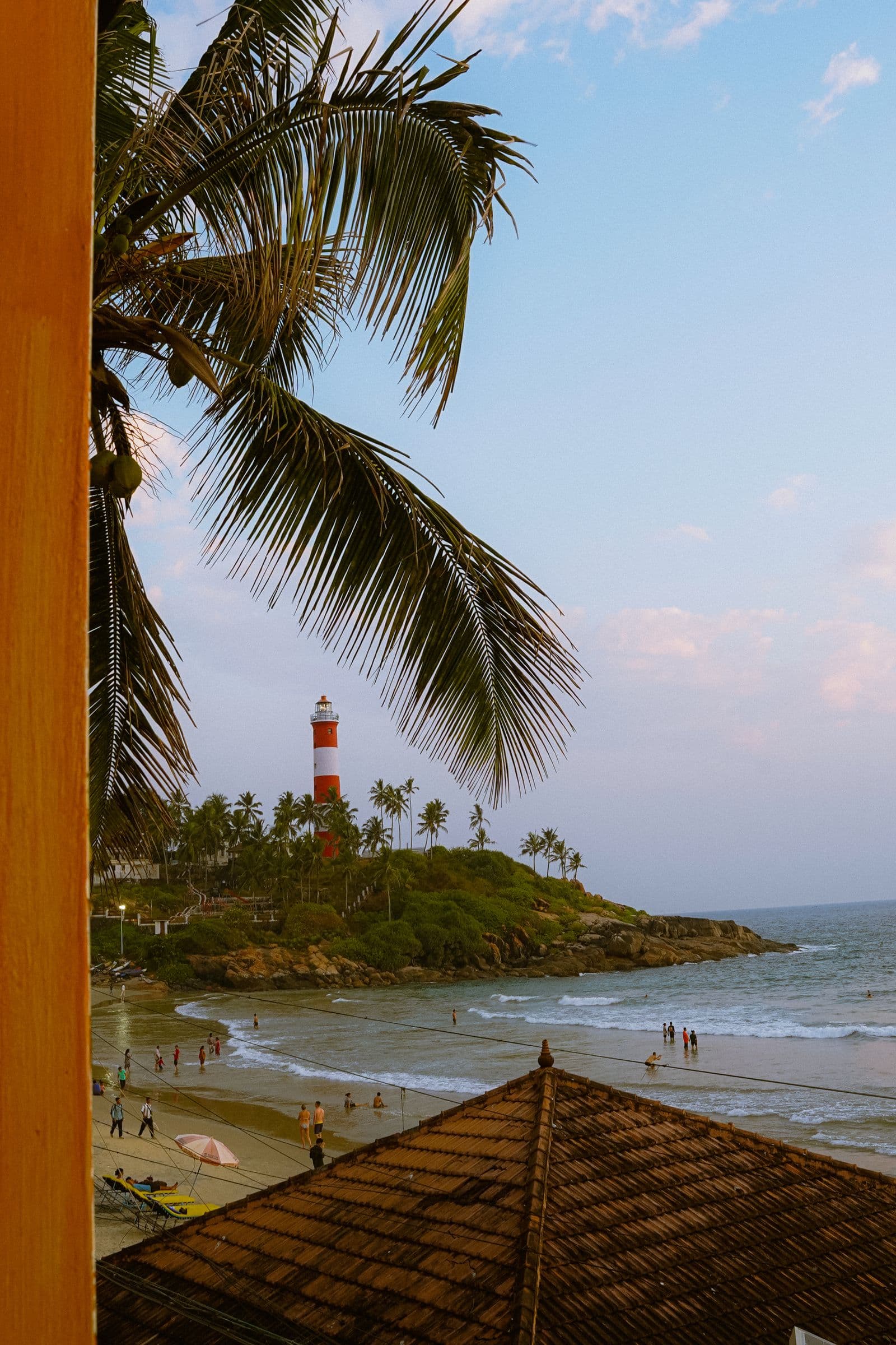 Palm-lined Kovalam Beach in Kerala with the red-and-white lighthouse on the headland