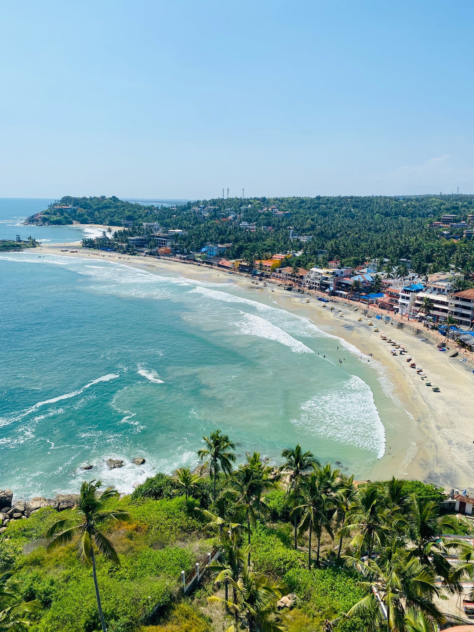Aerial view of the turquoise water and curving sand of Kovalam Beach, Kerala
