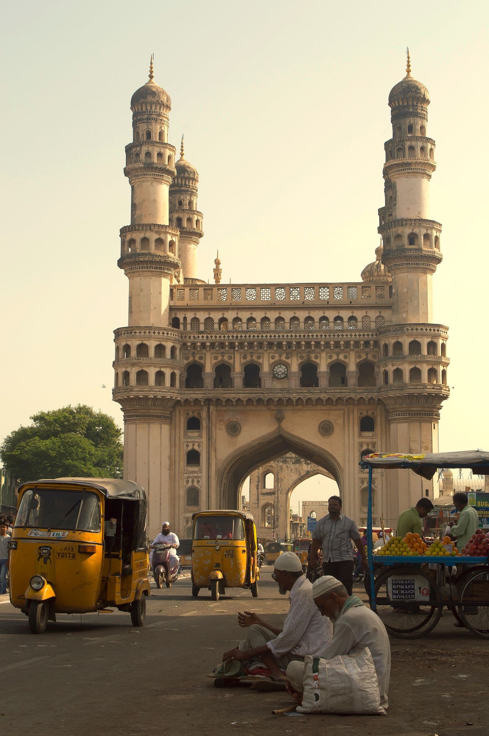 People walking on the street beside a large beige stone monument in Hyderabad