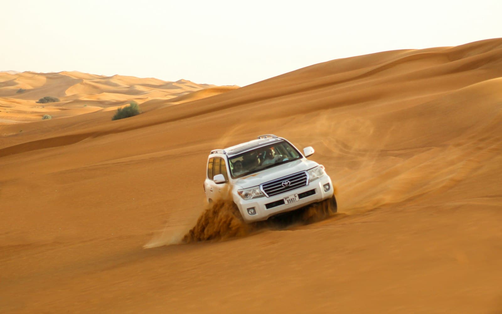 White 4x4 climbing an orange sand dune on a Dubai desert safari