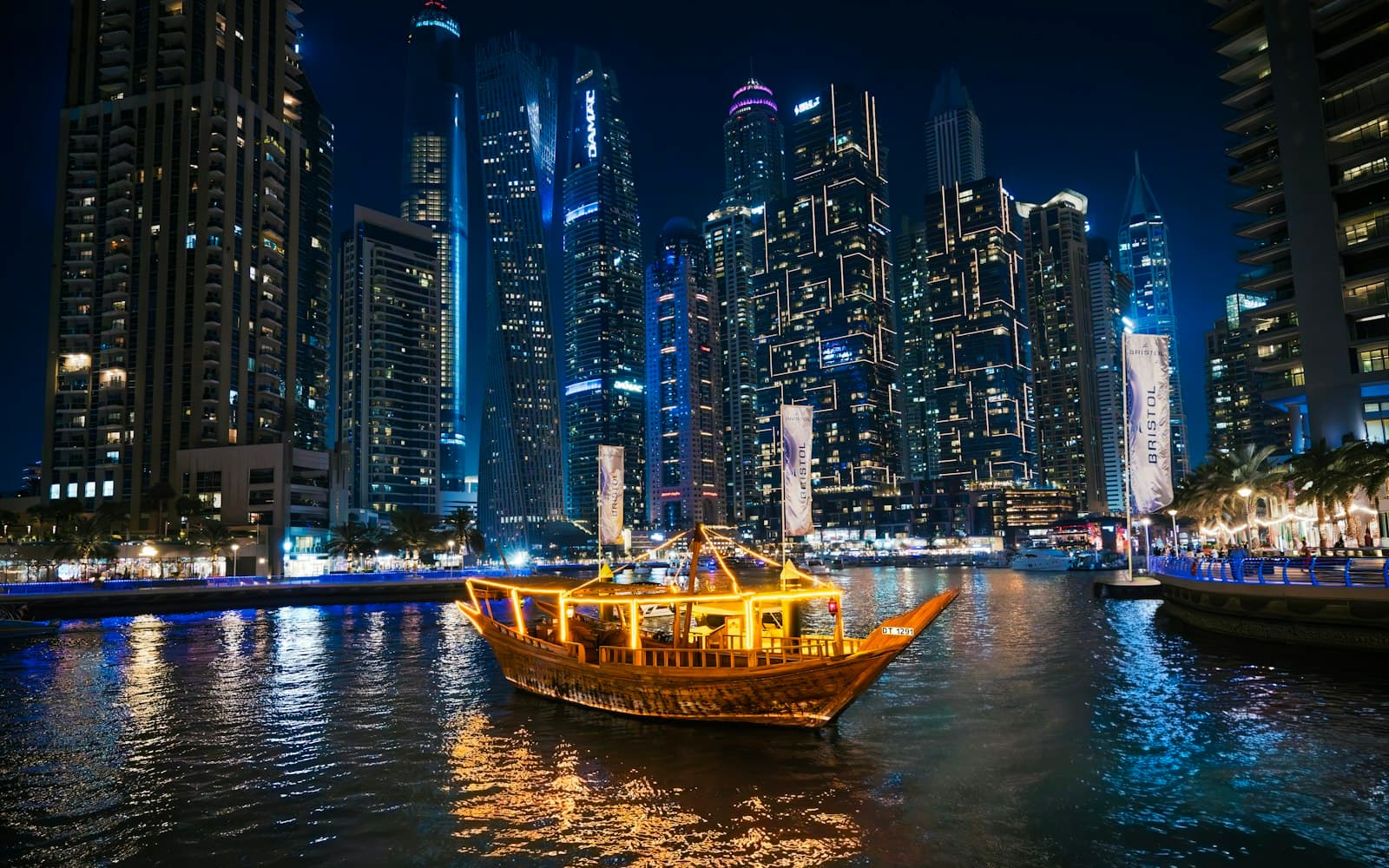 A wooden dhow cruise boat passing the lit towers of Dubai Marina at night