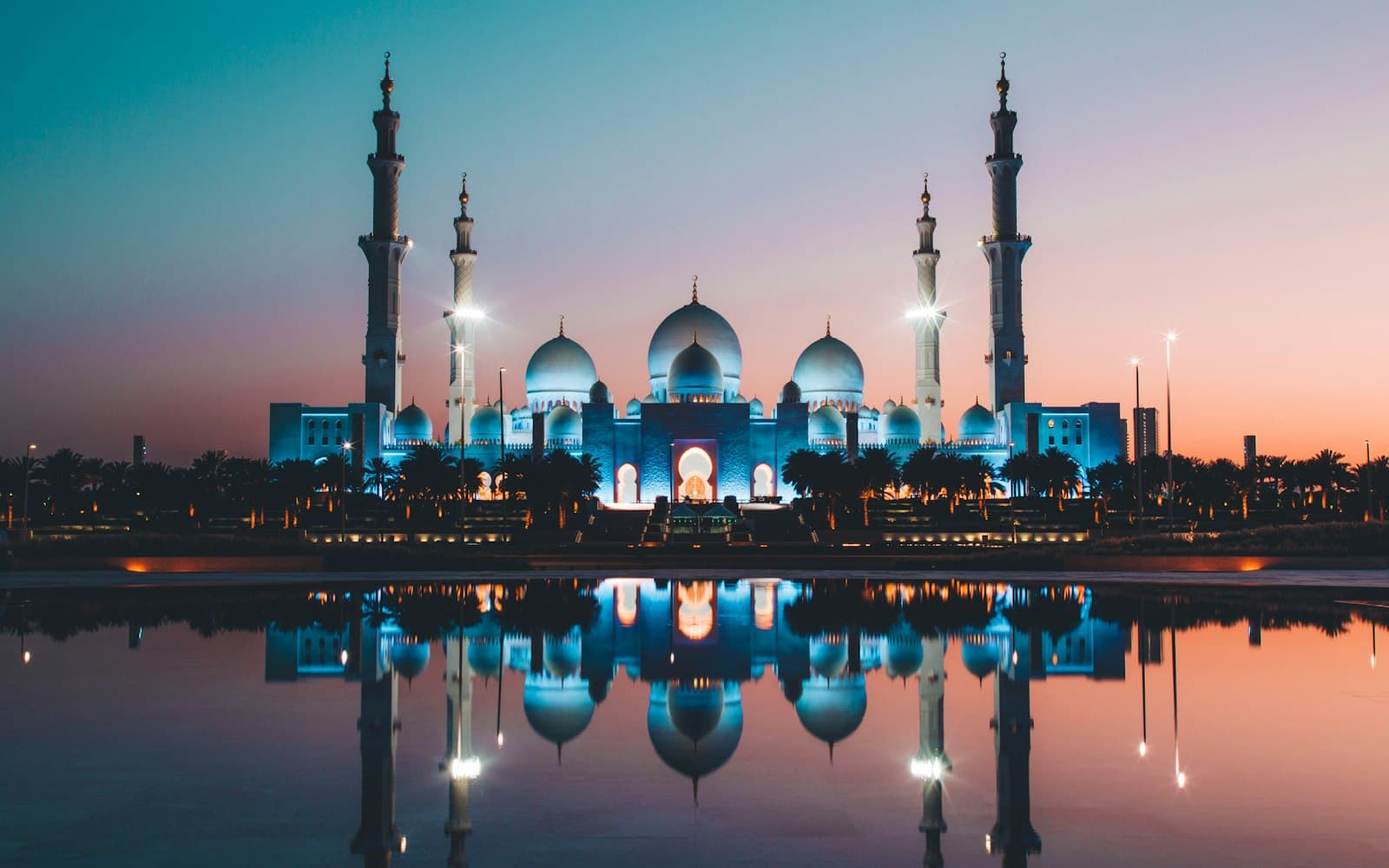 The Sheikh Zayed Grand Mosque lit up at dusk and reflected in its pools