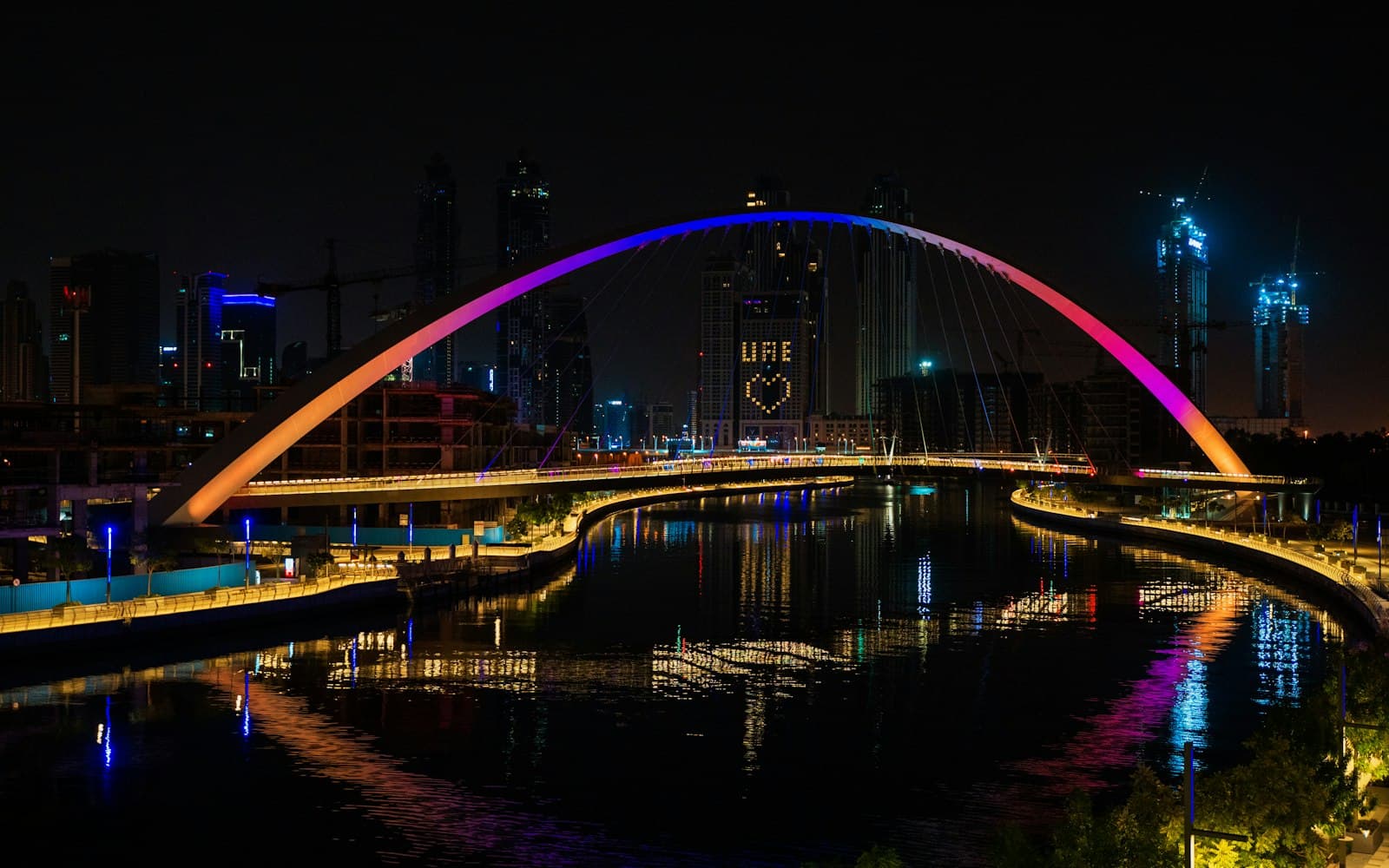 The arched Tolerance Bridge lit in purple and blue over the Dubai Water Canal